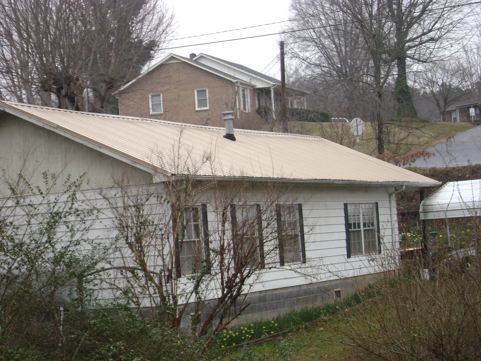 Tan metal roof on a white sided house set into a hillside — Commercial Roofing by Roofing Brothers in Palm Beach Gardens