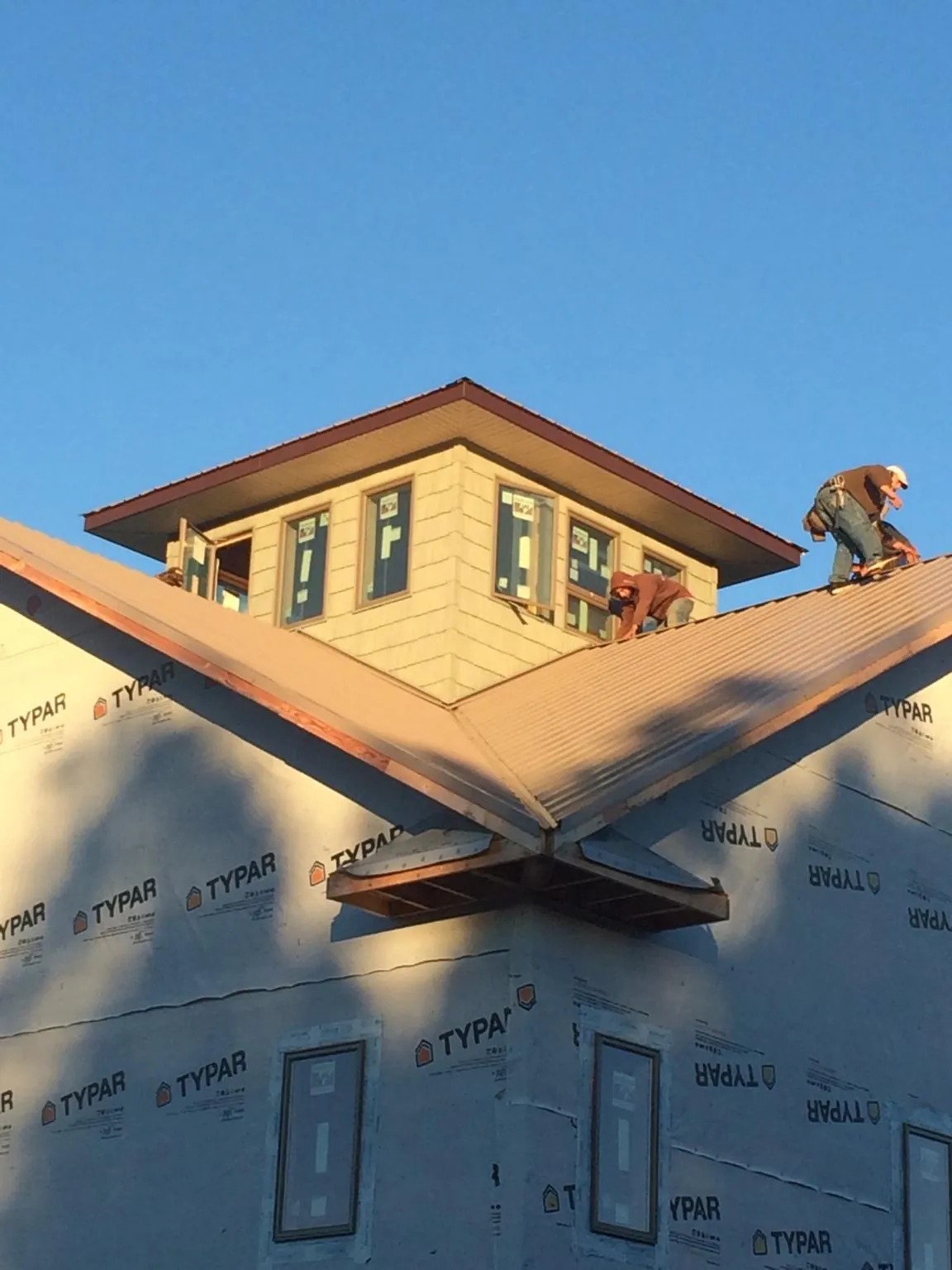 Roofers working around a rooftop cupola on a new metal roof at sunset — Roof Waterproofing in Palm Beach Gardens by Roofing Brothers